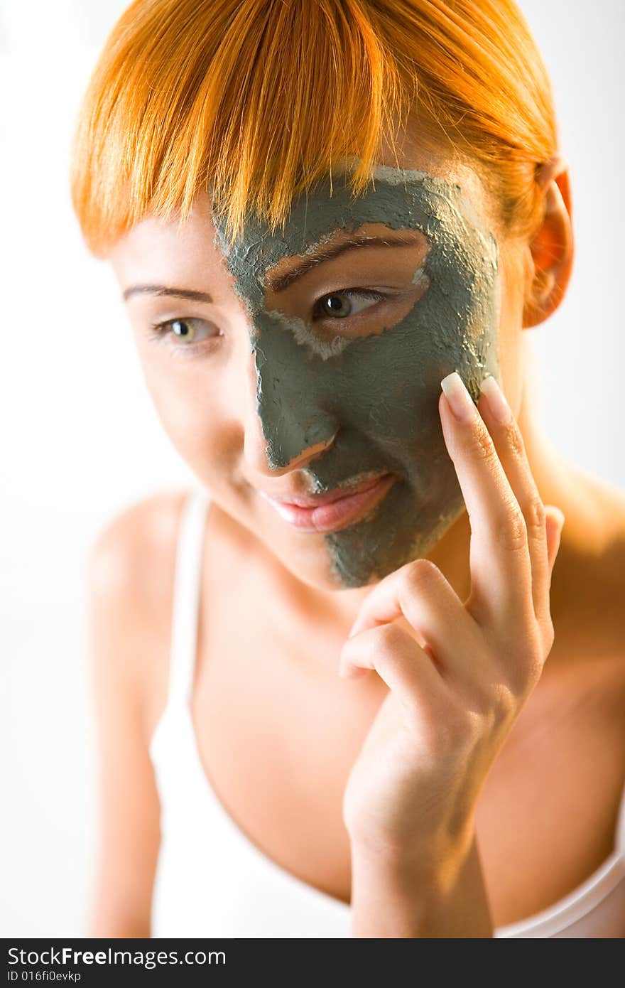 Young red-haired woman put green mask on half face. She's smiling and looking at camera. Closeup on face. Young red-haired woman put green mask on half face. She's smiling and looking at camera. Closeup on face.