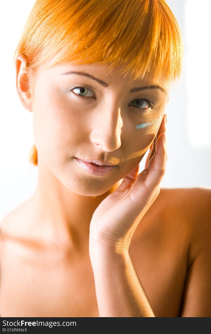 Young red-haired woman put cream on face. She's smiling and looking at camera. Front view. Closeup on face. Young red-haired woman put cream on face. She's smiling and looking at camera. Front view. Closeup on face.