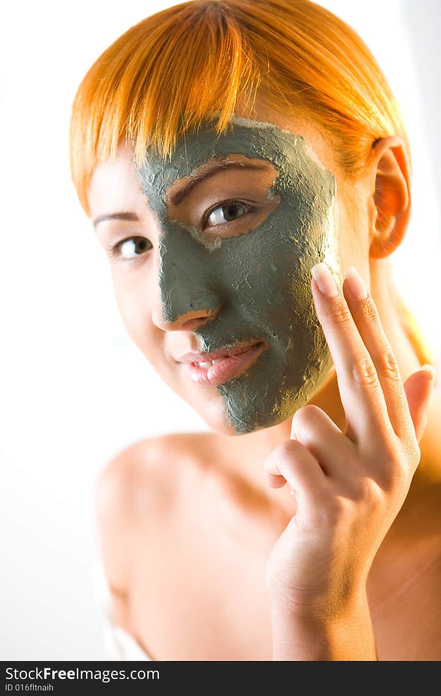 Young red-haired woman put green mask on half face. She's smiling and looking at camera. Closeup on face. Young red-haired woman put green mask on half face. She's smiling and looking at camera. Closeup on face.