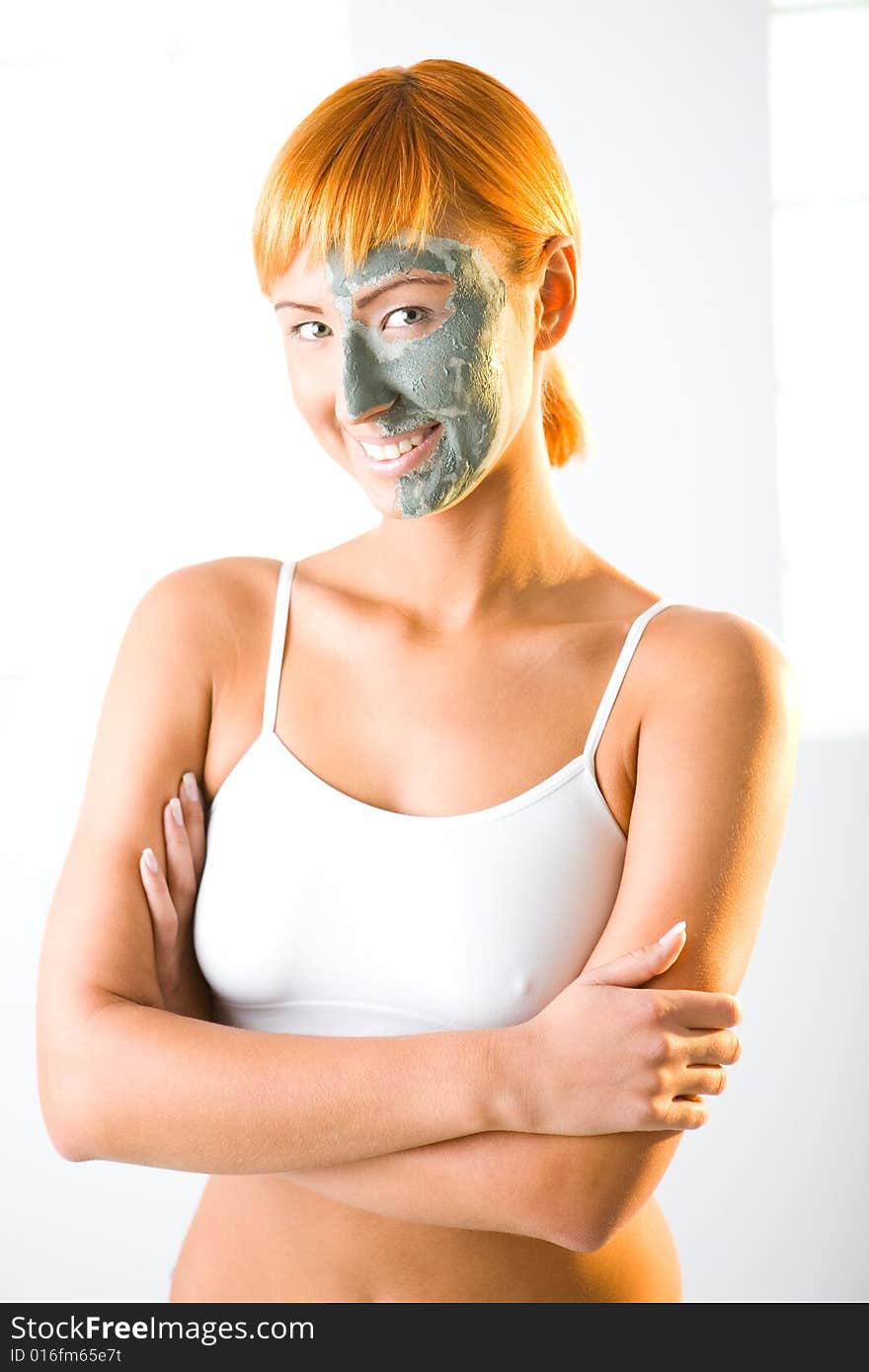 Young red-haired woman with green mask on half face. She's standing with crossed hands and smiling. Looking at camera. Young red-haired woman with green mask on half face. She's standing with crossed hands and smiling. Looking at camera.