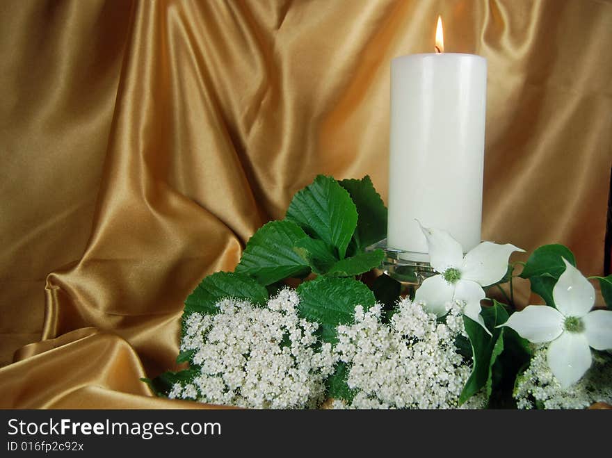 Glowing candle and dogwood on gold satin. Glowing candle and dogwood on gold satin.