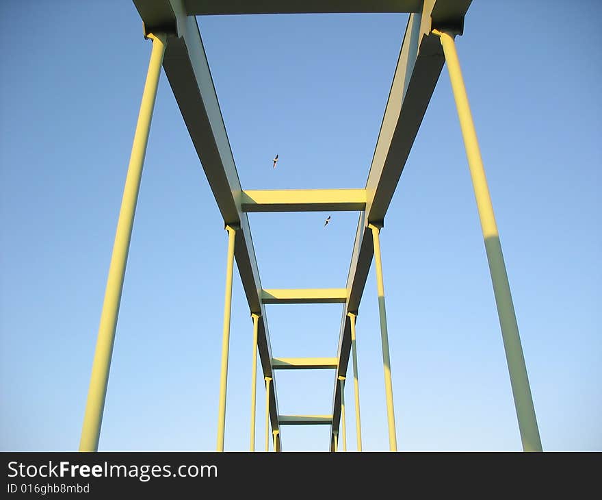 Bridge with two sea gulls flowing over it.