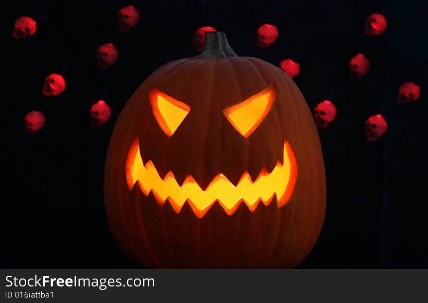 A lone jack-o-lantern grins maniacally on a pitch black Halloween night, red disembodied skulls dance in the background. A lone jack-o-lantern grins maniacally on a pitch black Halloween night, red disembodied skulls dance in the background