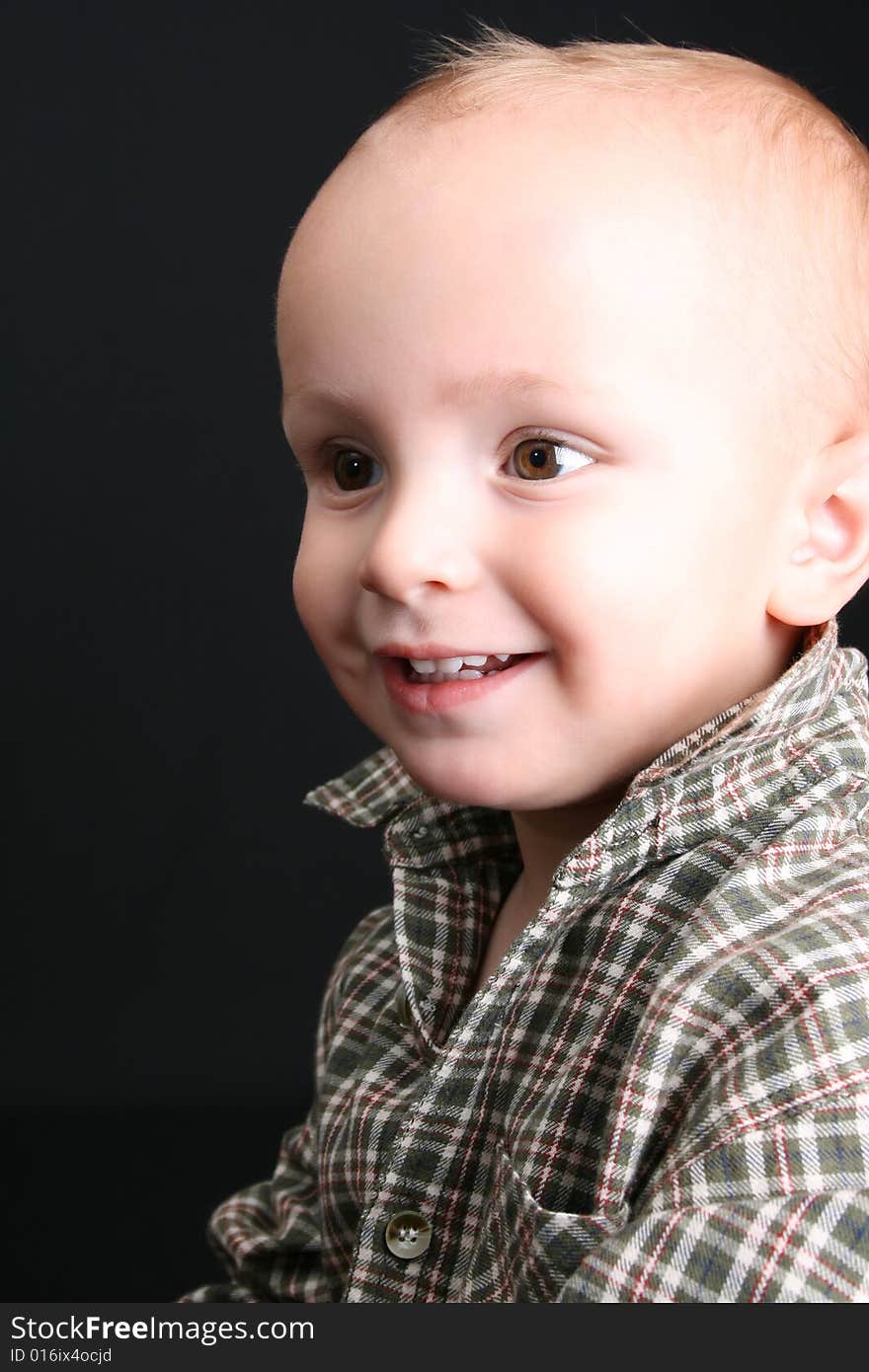 Blonde toddler against a black background with a smile