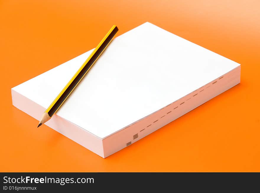 Blank book and pencil over an orange background