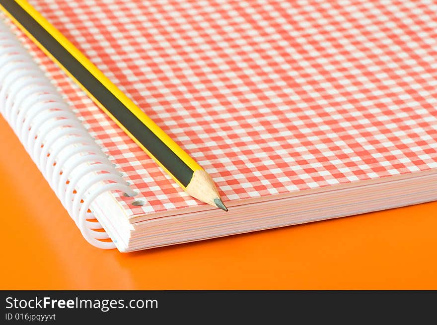 Pencil and notebook over an orange background. Pencil and notebook over an orange background