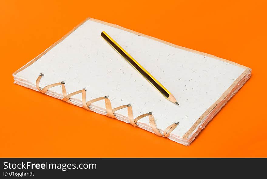 Recycled notepad and pencil over an orange background. Recycled notepad and pencil over an orange background