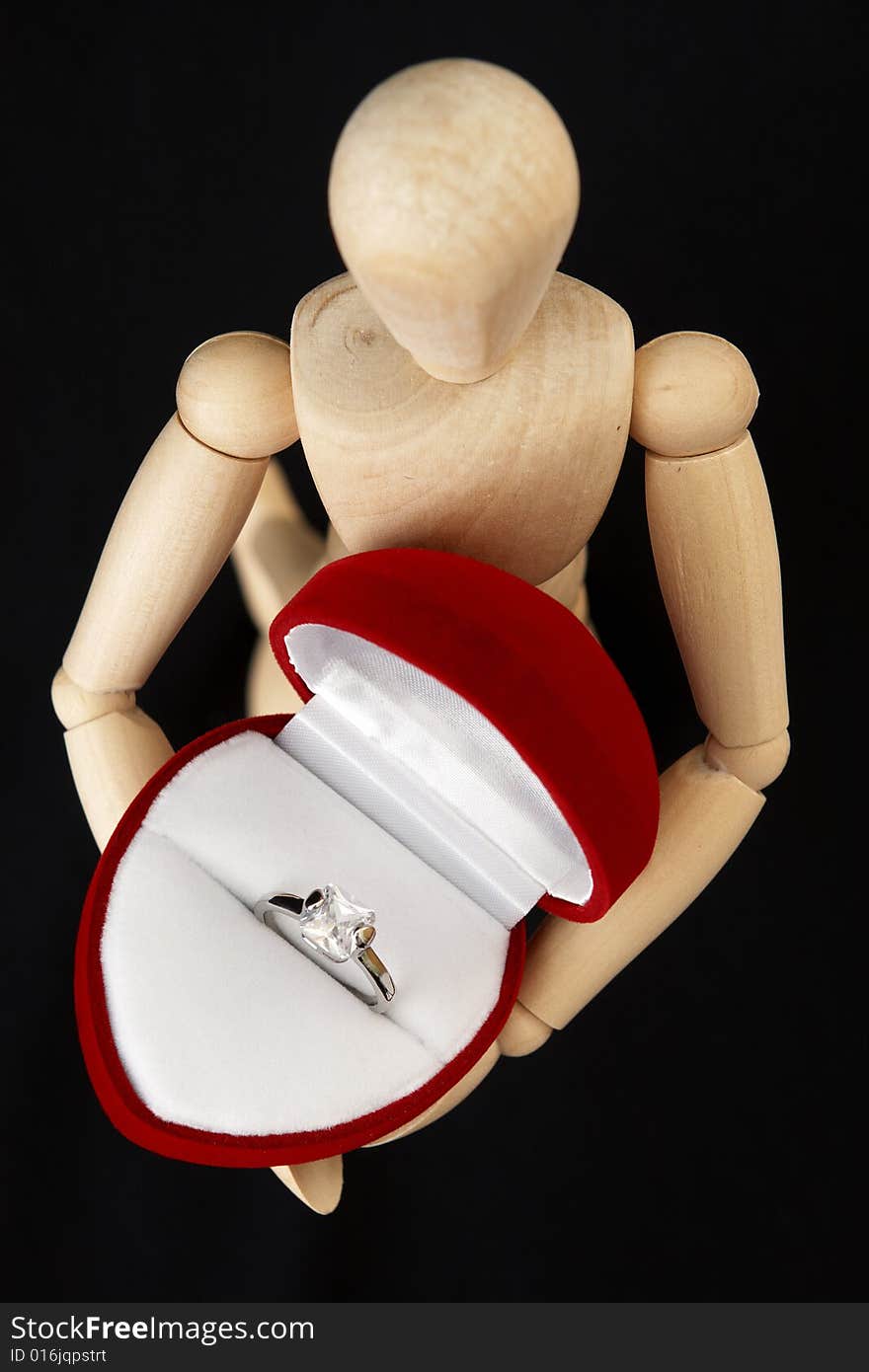 A beautiful crystal white engagement ring in a red juwelery box , held by a wooden mannequin. A beautiful crystal white engagement ring in a red juwelery box , held by a wooden mannequin