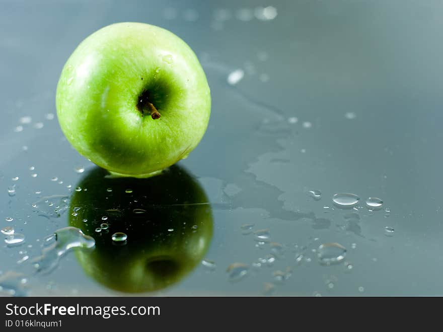 An apple reflecting on a glass surface with water drops around it