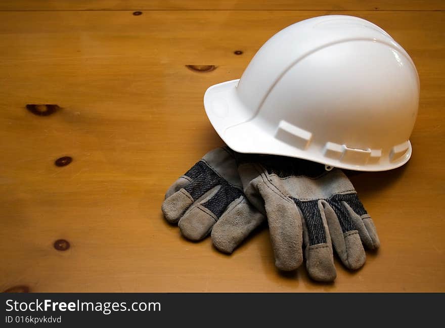 White hard hat and gloves resting on a wood surface. White hard hat and gloves resting on a wood surface