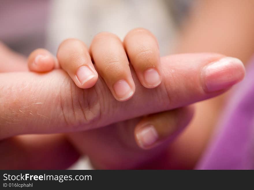 Tiny newborn baby fingers wrapped around adult female fingers up close. Tiny newborn baby fingers wrapped around adult female fingers up close