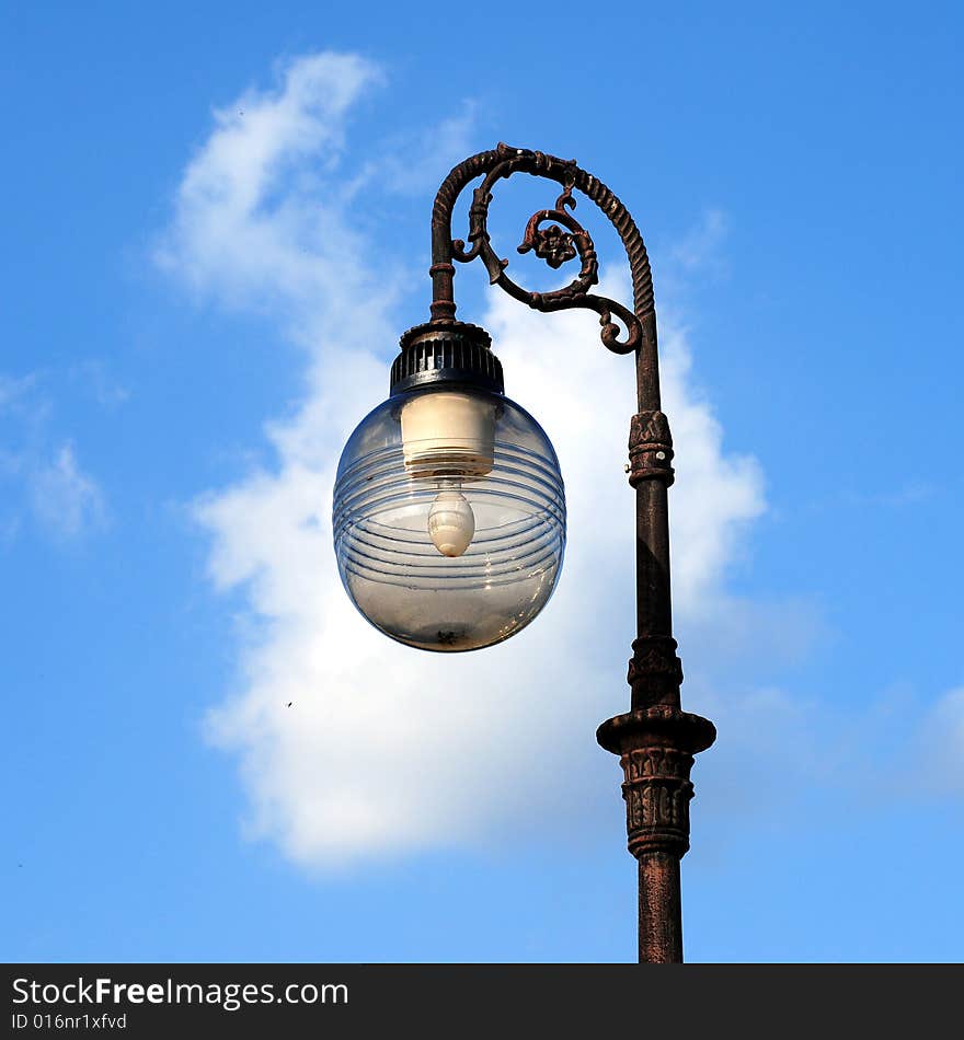 Three ornate street lamps on a lamp post against a blue sky in Romania