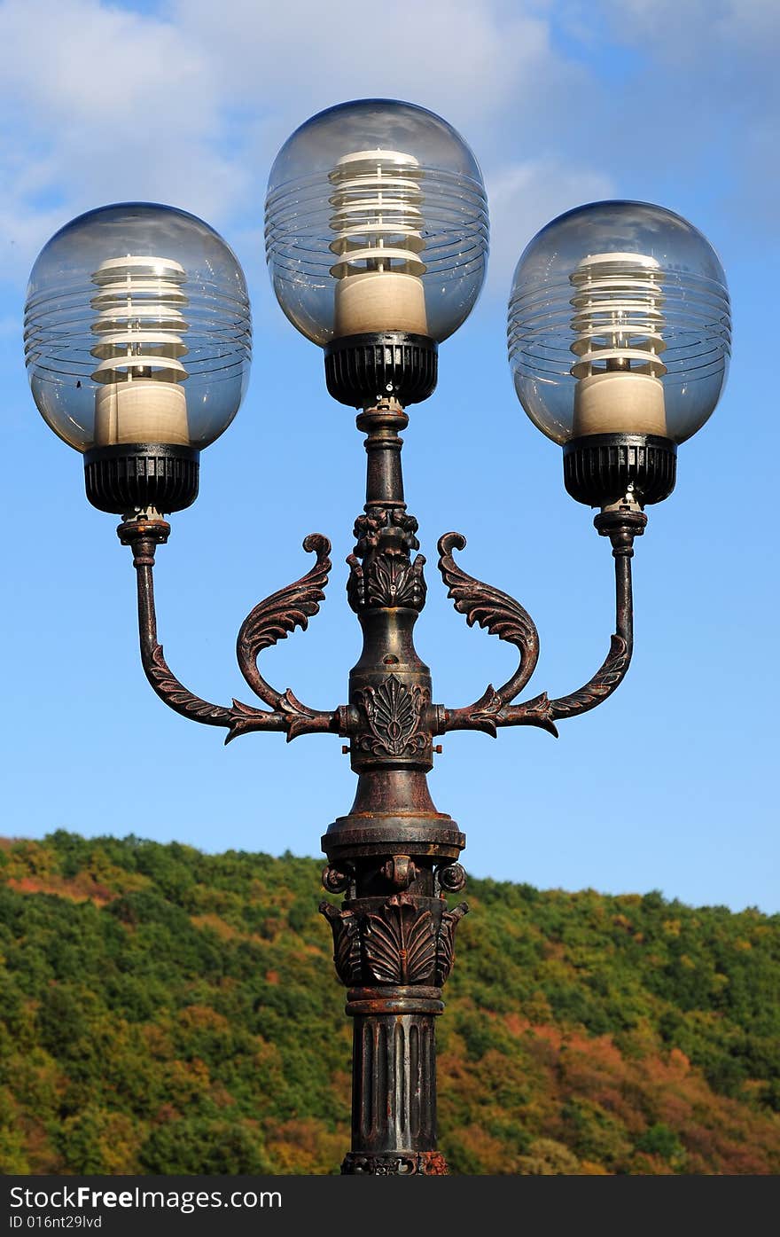 Three ornate street lamps on a lamp post against a blue sky in Romania