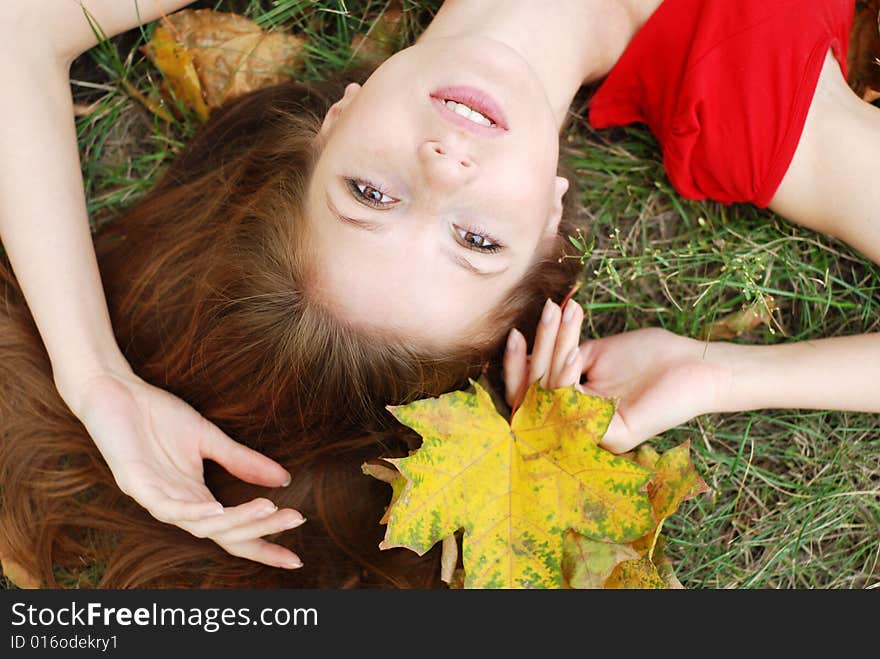 Young beautiful woman lying on the green grass with maple leaf. Young beautiful woman lying on the green grass with maple leaf