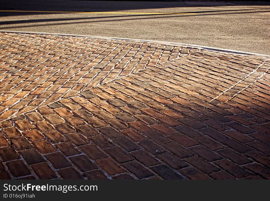 Sunsetting on old brick sidewalk casting deep shadows also showing street. Sunsetting on old brick sidewalk casting deep shadows also showing street