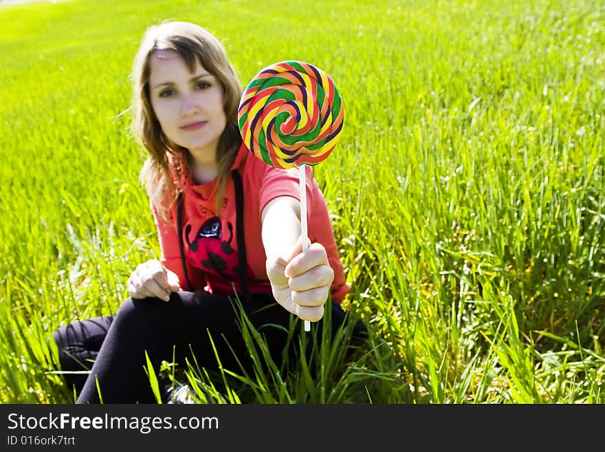 Blonde cutie behind spiral candy on green background. Focus on candy. Blonde cutie behind spiral candy on green background. Focus on candy.