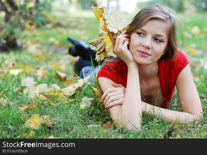 Young beautiful woman lying on the green grass with maple leaf. Young beautiful woman lying on the green grass with maple leaf