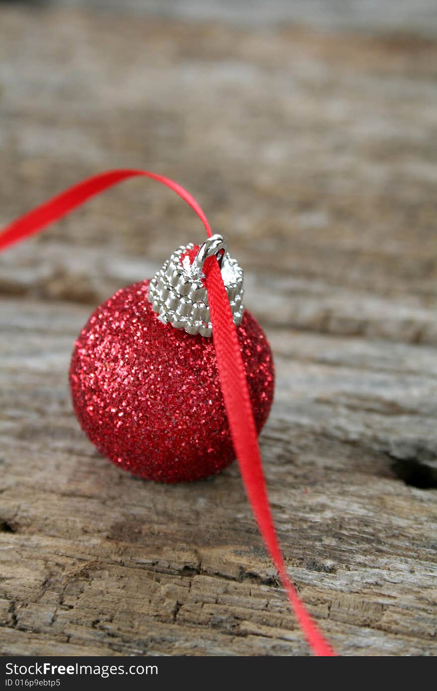 A red Christmas ornament with a red ribbon on an old piece of wood for a rustic look.  A soft focus effect to add a bit of elegance also copy space available.