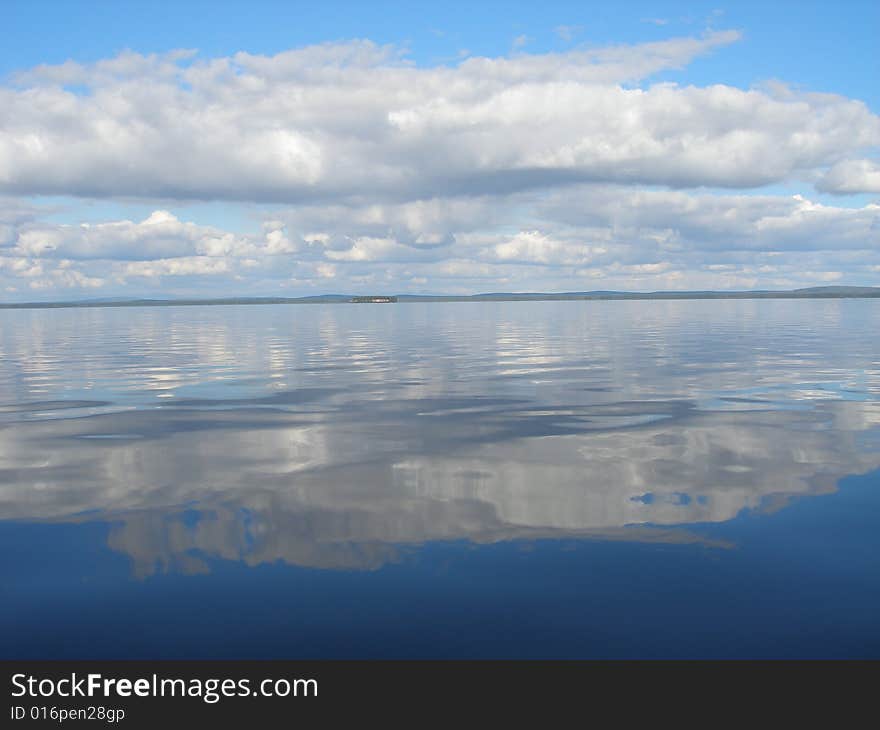 Bright blue sky and reflection of it and the clouds in clear lake water. Bright blue sky and reflection of it and the clouds in clear lake water