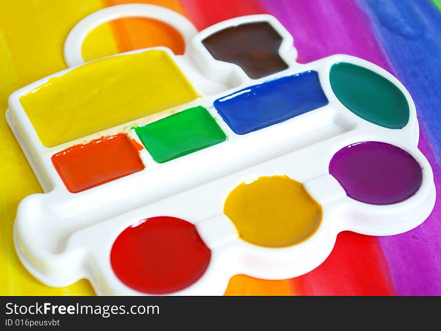 Box of watercolors and a brush on a colorful  background