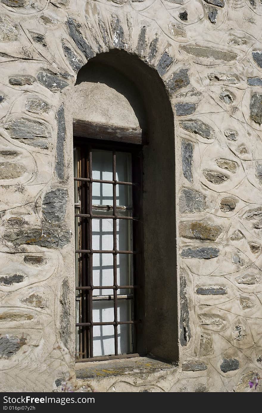 Old window with bars on a masonry wall with built in stones