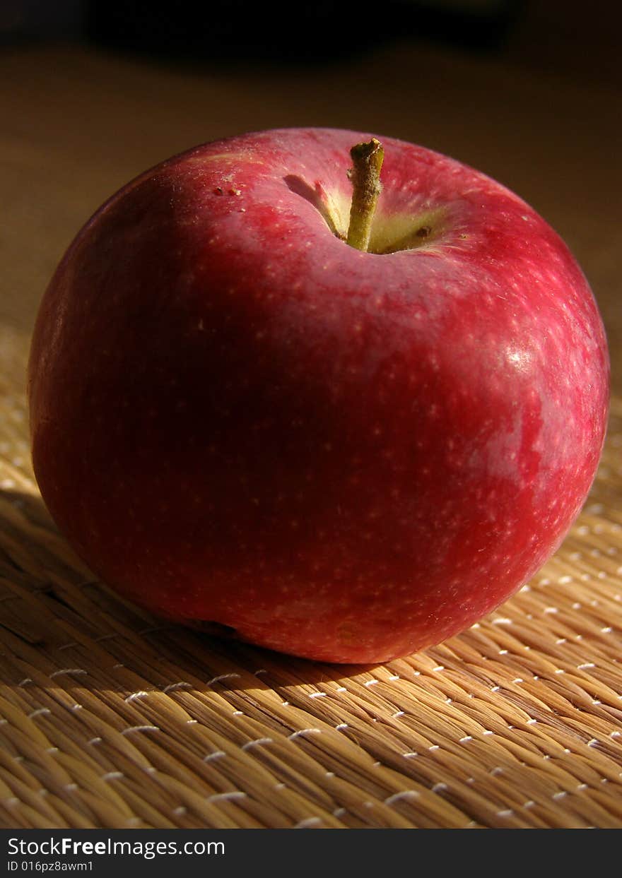 Red ripe apple lies on the mat. Apple is illuminated by the sunlight. Red ripe apple lies on the mat. Apple is illuminated by the sunlight