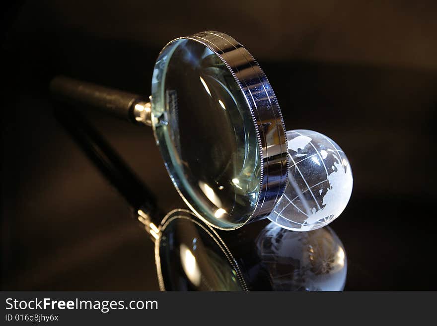 Close-up of magnifier and little glassy earth on dark background. Close-up of magnifier and little glassy earth on dark background