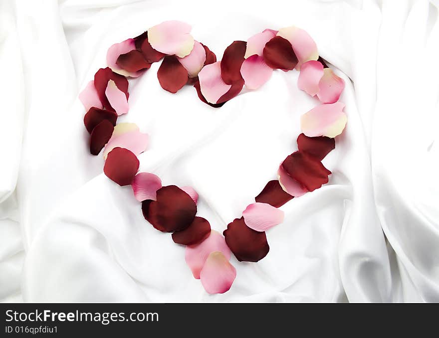 Symbol of heart from rose-petals on white silk