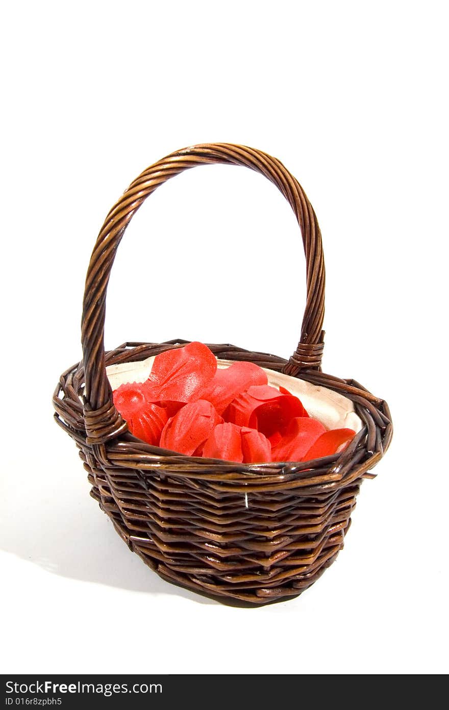 Wicker basket filled with red rose peddles on a white background