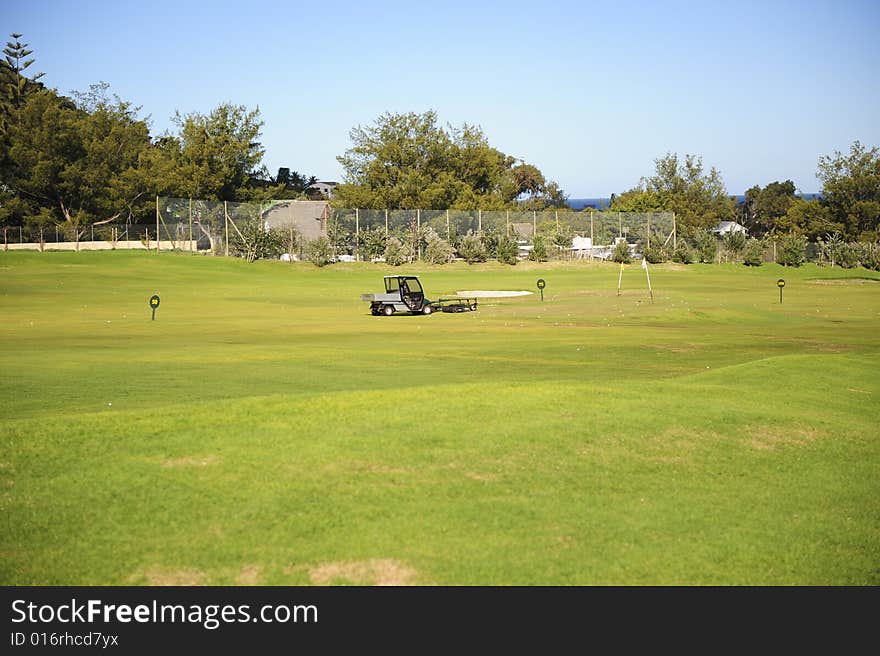 A beautifully maintained practice or driving range with distance markers for golfers to practice on. A motorized vehicle is in the process of picking up balls on the range. A beautifully maintained practice or driving range with distance markers for golfers to practice on. A motorized vehicle is in the process of picking up balls on the range.