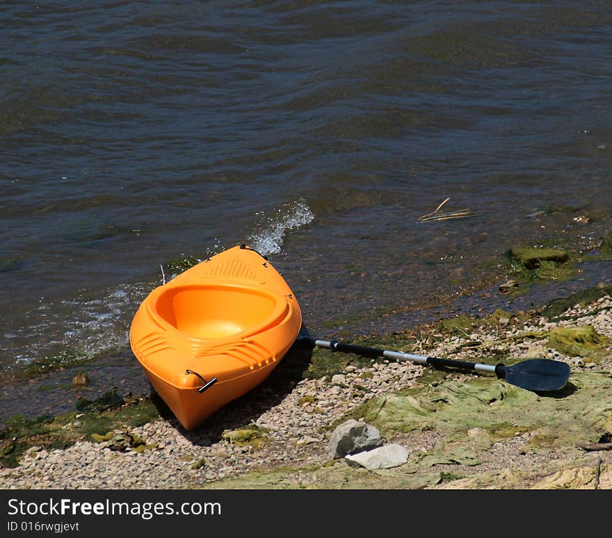 Orange kayak and paddle beached on lake shore