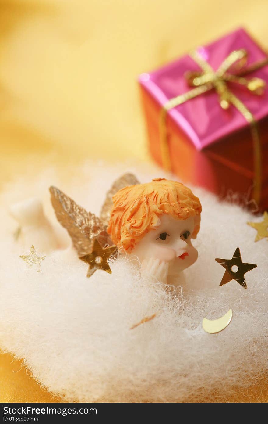 Angel on white cloud with golden stars and christmas gift with golden ribbon on golden background.