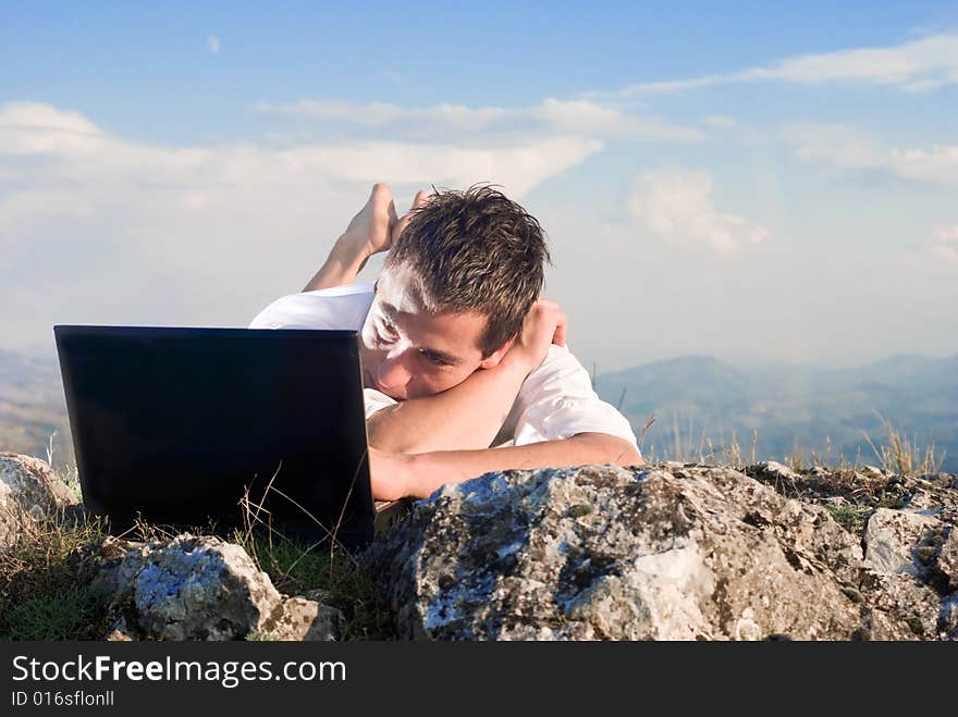 Young man using his laptop, lying on the rock. Young man using his laptop, lying on the rock