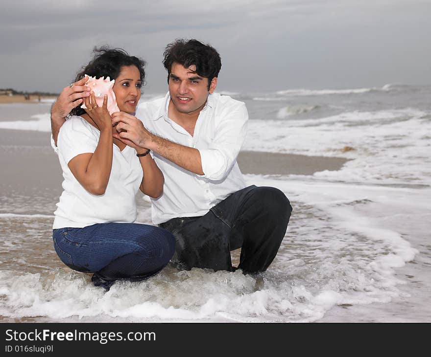 Asian couple of indian origin on the beach listening to a shell. Asian couple of indian origin on the beach listening to a shell