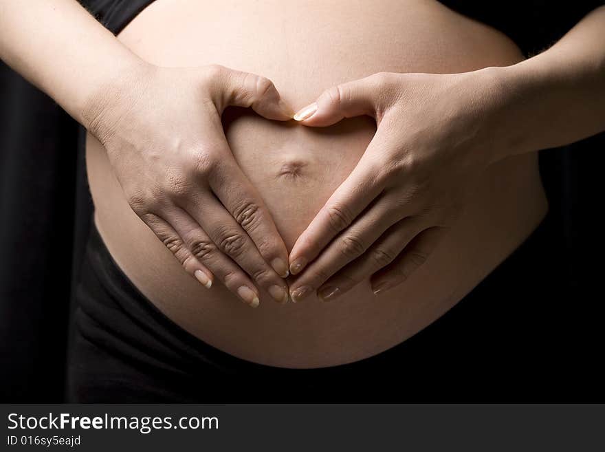 Lose-up of a belly with the hands of the happy future mother making a heart shape . Happy mother. Lose-up of a belly with the hands of the happy future mother making a heart shape . Happy mother