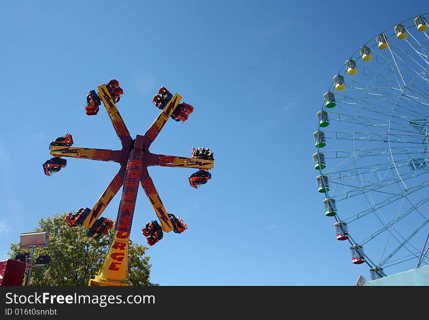 A carnival ride turns in circles against the blue sky.