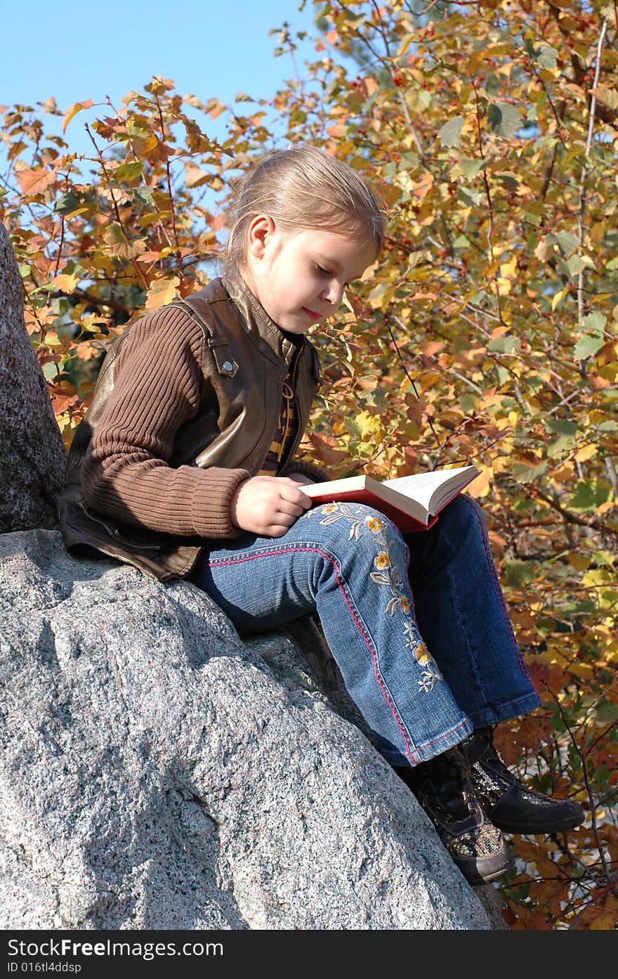 Little girl sitting on the stone and reading a book in the park. Little girl sitting on the stone and reading a book in the park