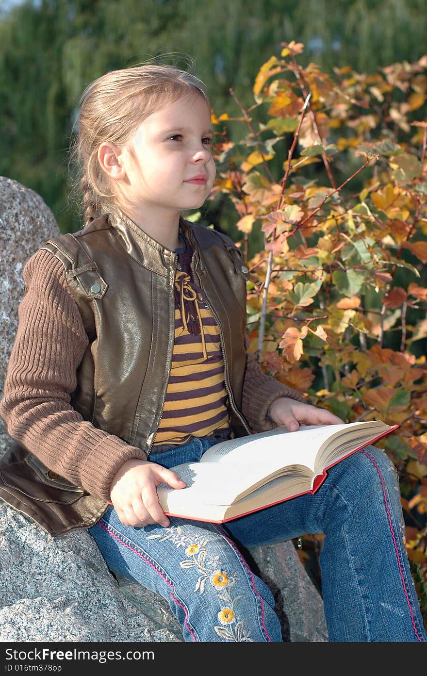 Little girl sitting on the stone and reading a book in the park. Little girl sitting on the stone and reading a book in the park