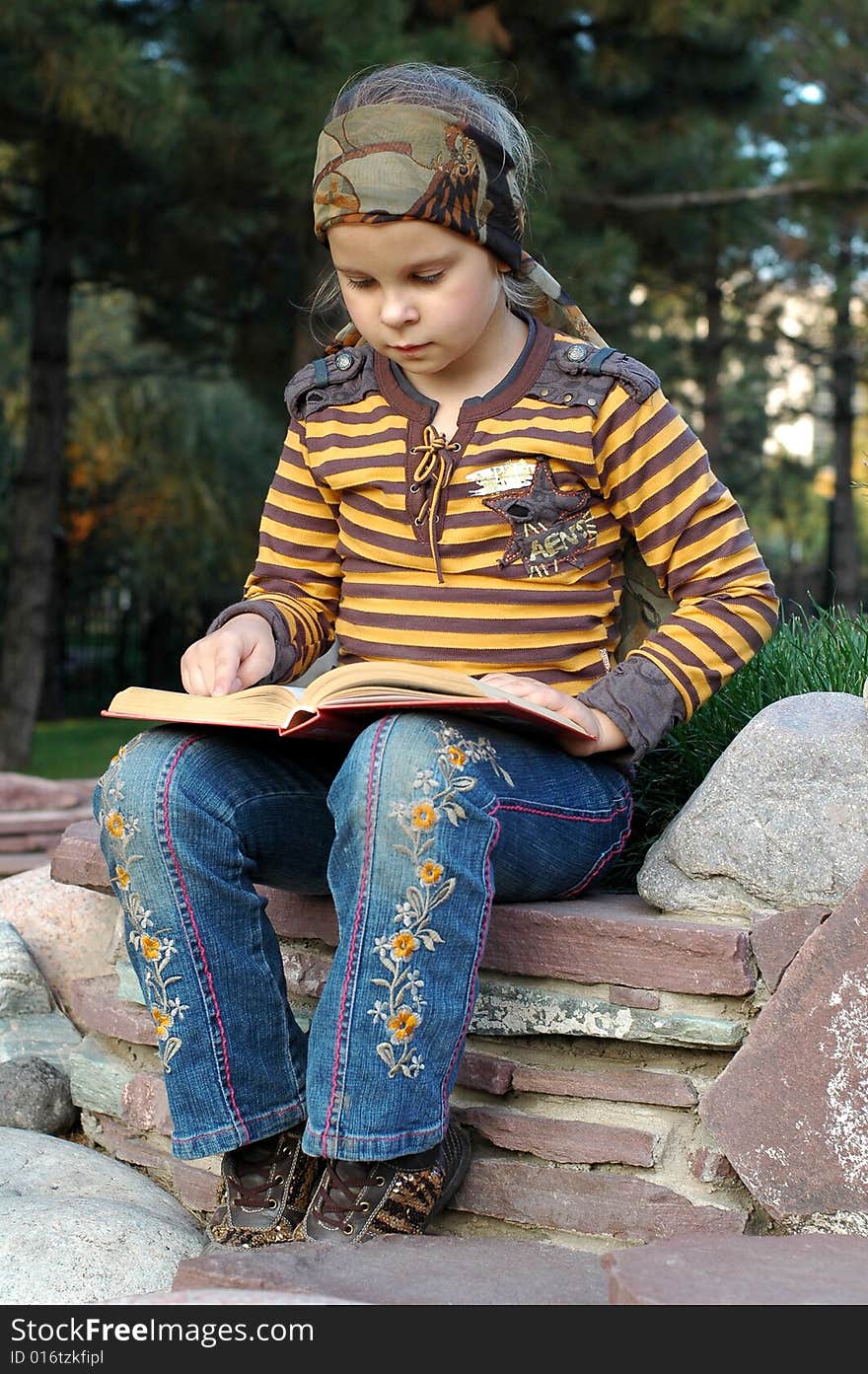 Little girl reading a book in the park