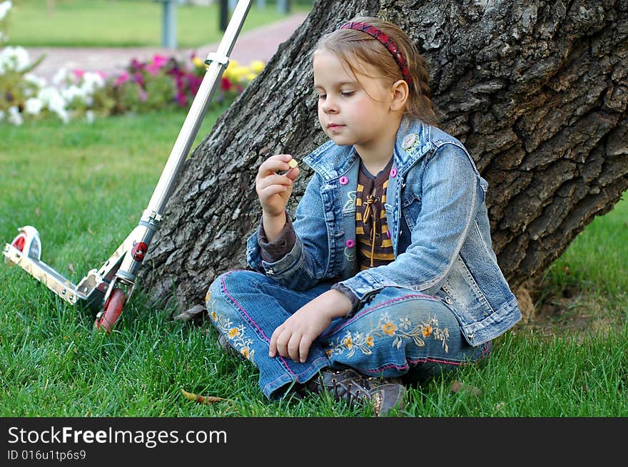 Little girl with scooter sitting under the tree. Little girl with scooter sitting under the tree