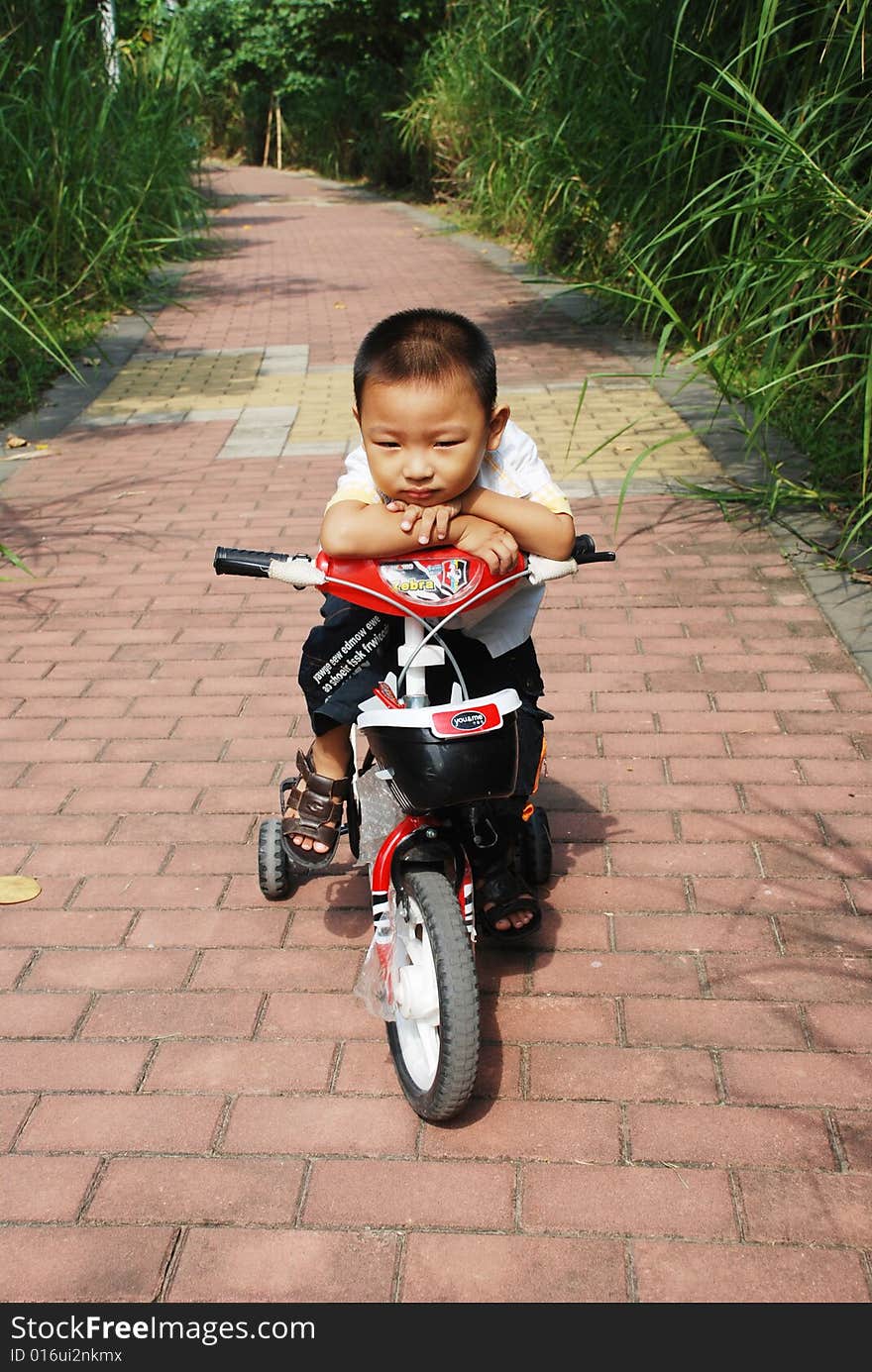 A naughty Chinese boy riding a bicycle on the footpath way in a park. A naughty Chinese boy riding a bicycle on the footpath way in a park.