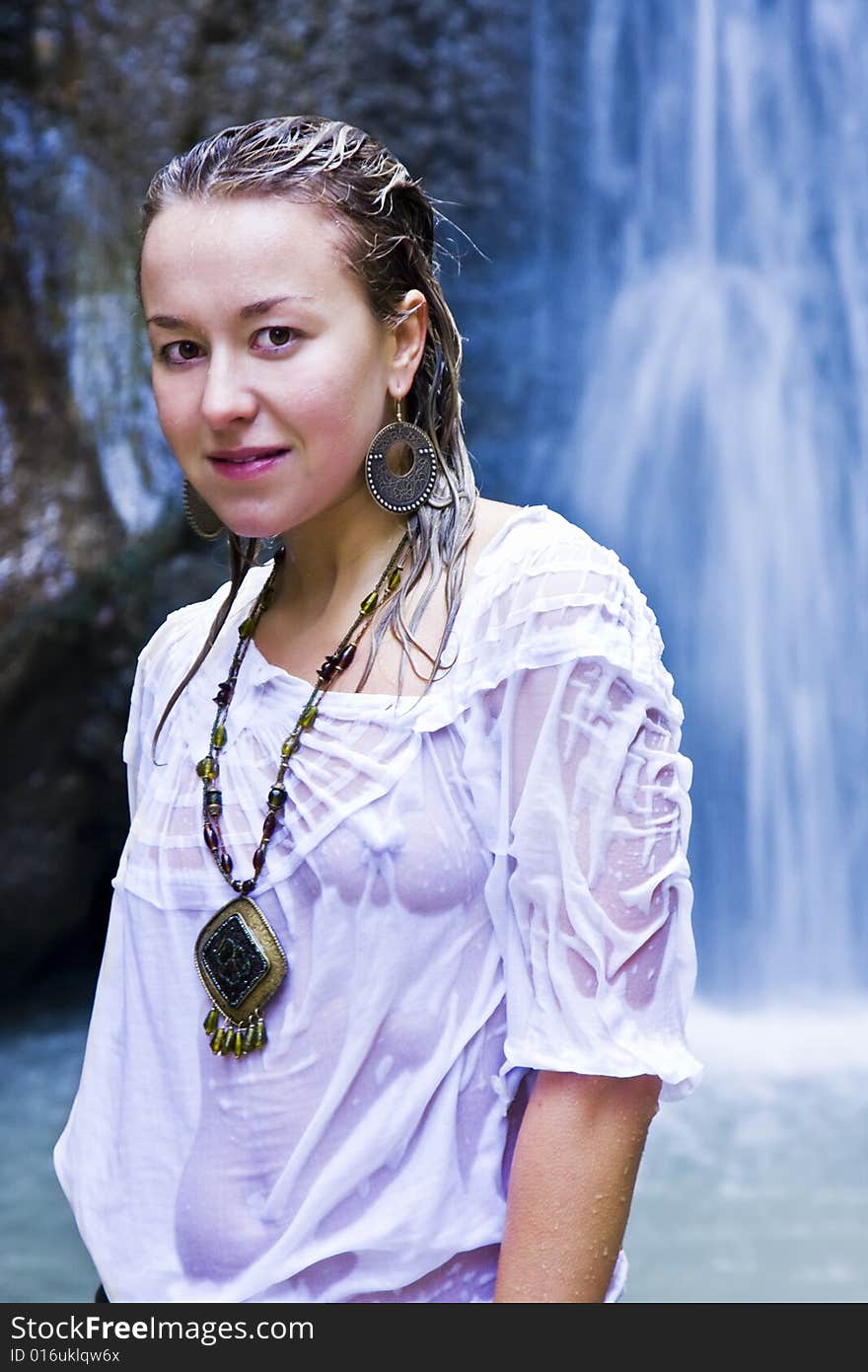 Young woman smiling at camera with blue waterfall as background. Young woman smiling at camera with blue waterfall as background