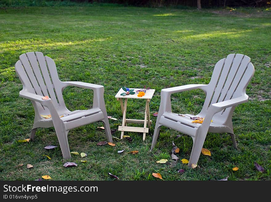 Two lounge chairs and a wooden table. Fall foliage, flowers, and berries scattered around. Two lounge chairs and a wooden table. Fall foliage, flowers, and berries scattered around.