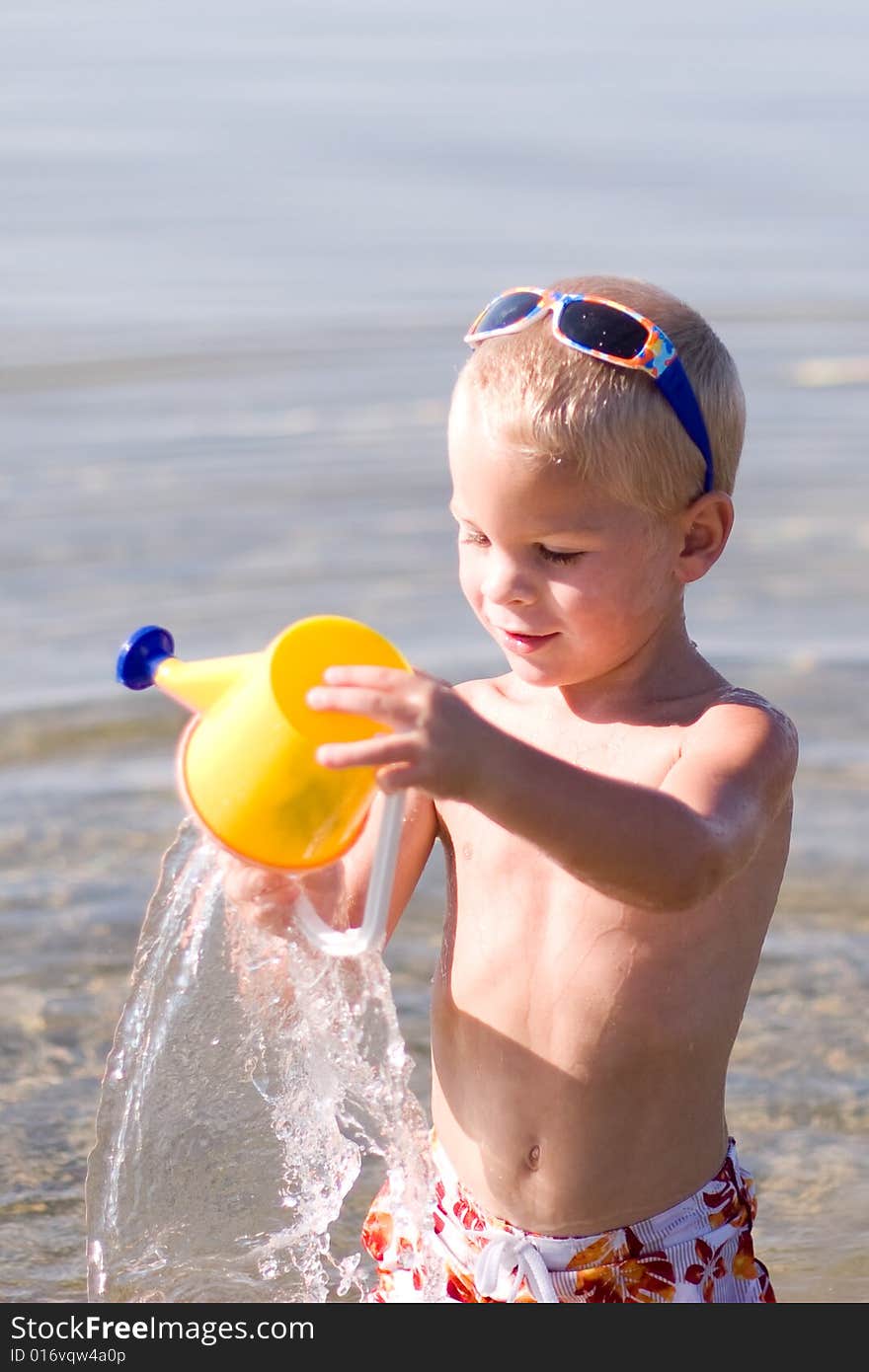 Boy pouring water from  his bucket at the beach