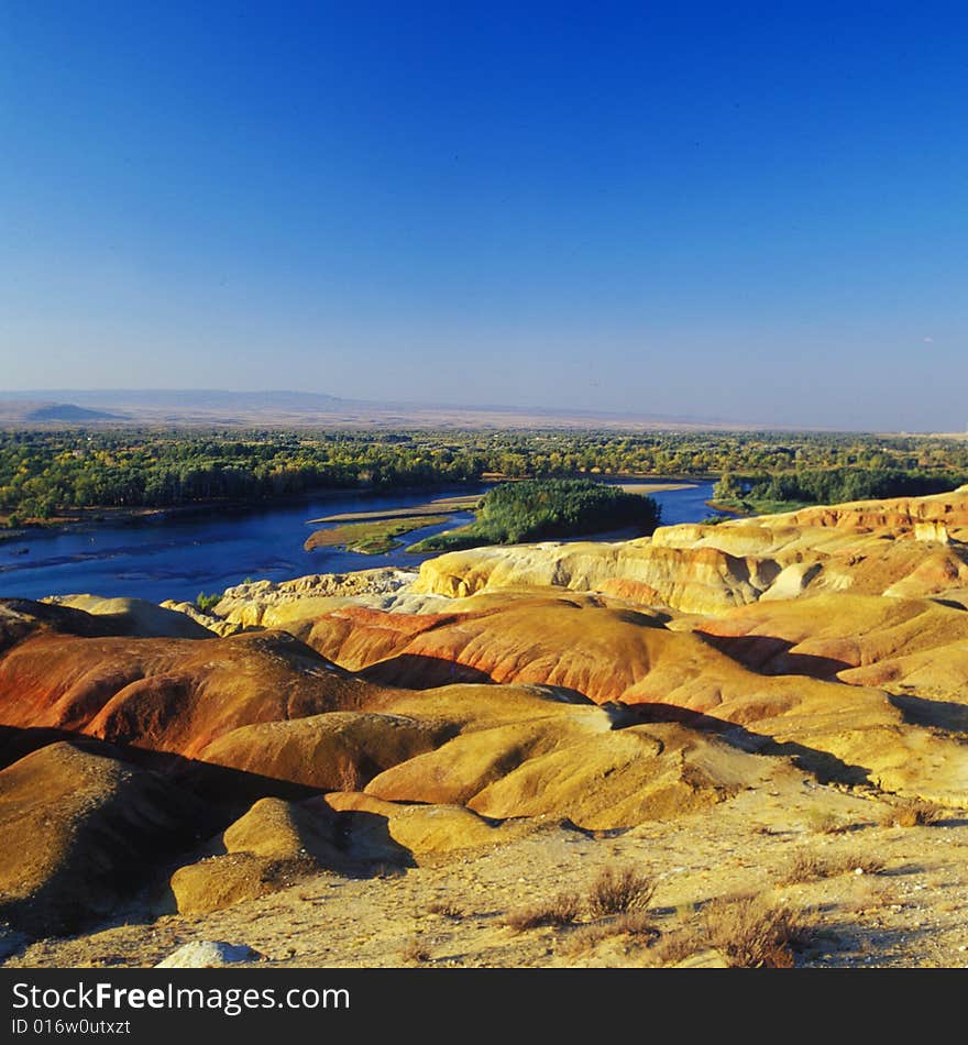 A river with forest and red rock on its sides . A view in Xinjiang China. A river with forest and red rock on its sides . A view in Xinjiang China