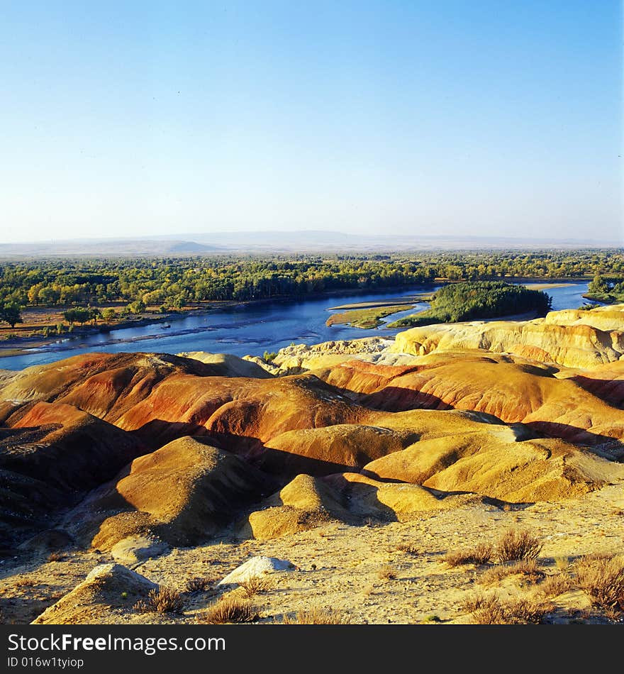 A river with forest and red rock on its sides . A view in Xinjiang China. A river with forest and red rock on its sides . A view in Xinjiang China