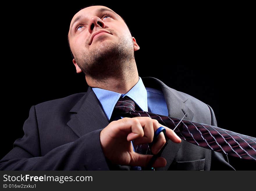 Man in a business suit scissors the tie, on a black background. Man in a business suit scissors the tie, on a black background