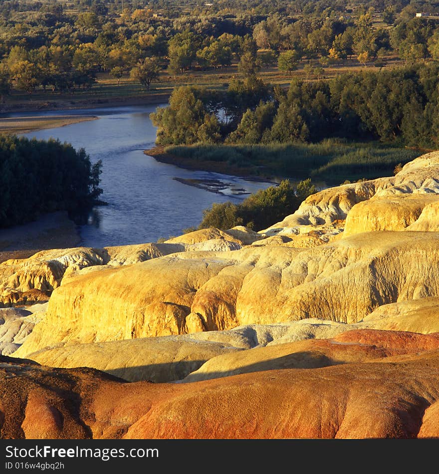 A river with forest and red rock on its sides . A view in Xinjiang China. A river with forest and red rock on its sides . A view in Xinjiang China