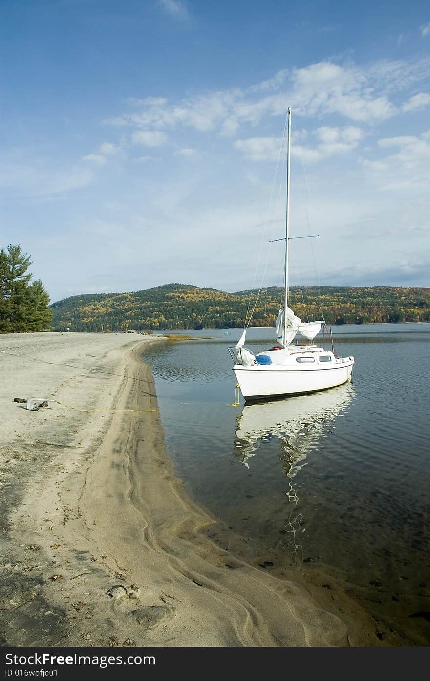 A small white sail boat near the shore