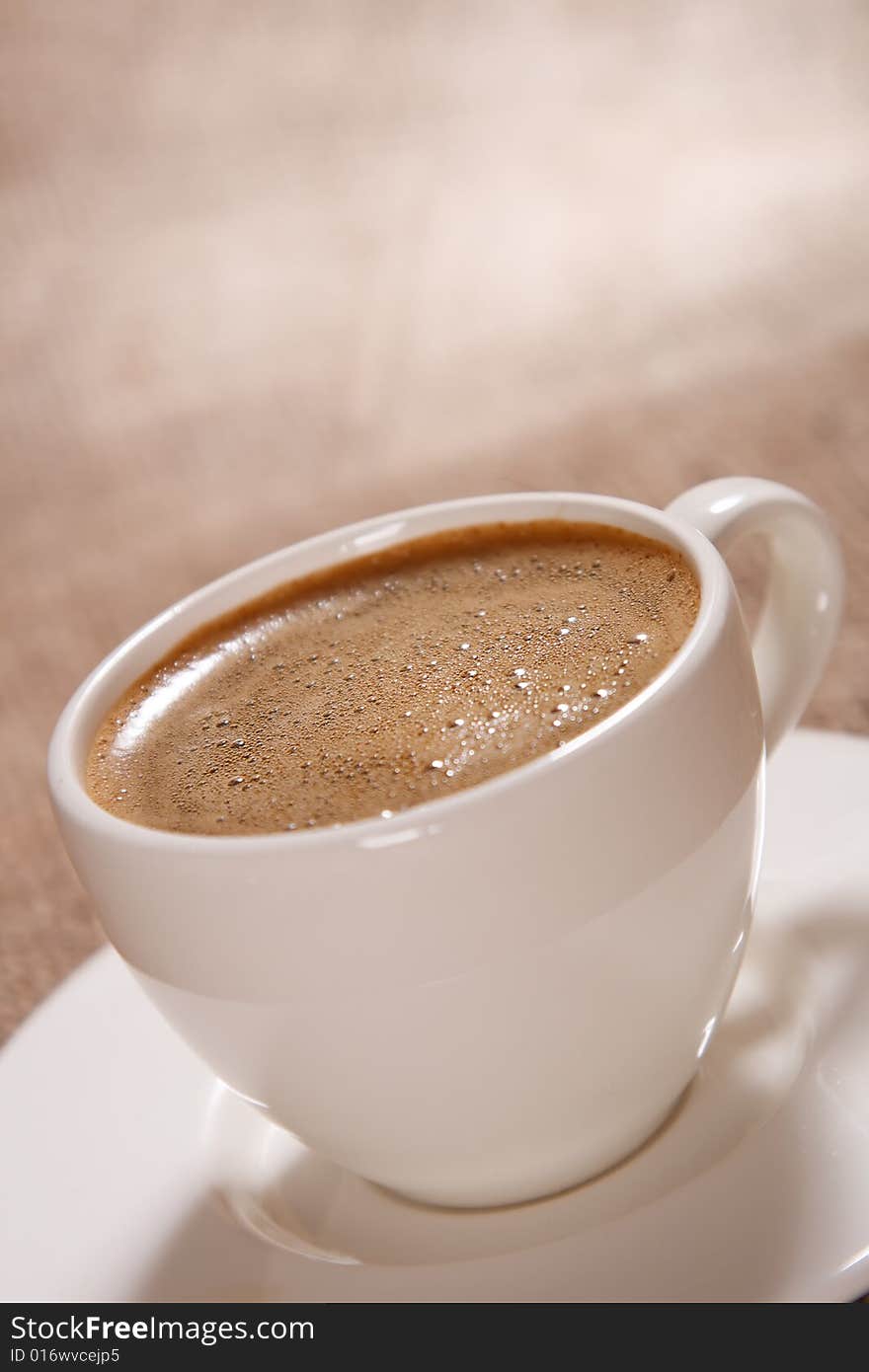 Cup of black coffee with froth on brown background